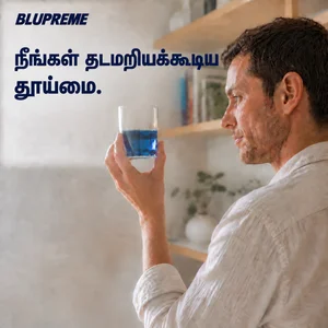 நீலத் திரவம் உள்ள கண்ணாடிக் கோப்பையைப் பிடித்திருக்கும் நபர்